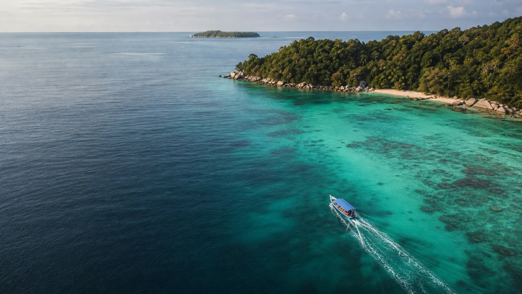 A small passenger boat crossing clear water beside a forested Terengganu island.